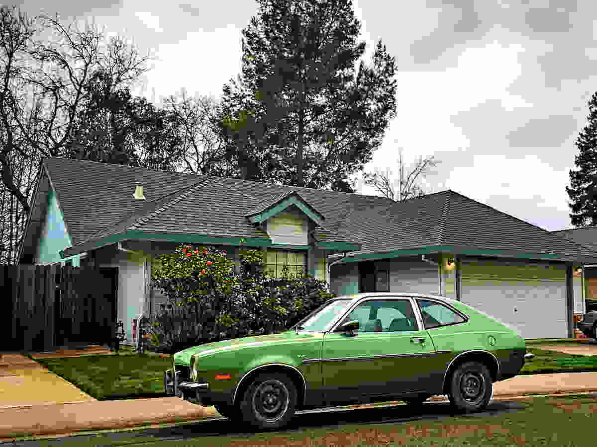 One-story house with an old used Ford Pinto sitting in front of it, California.